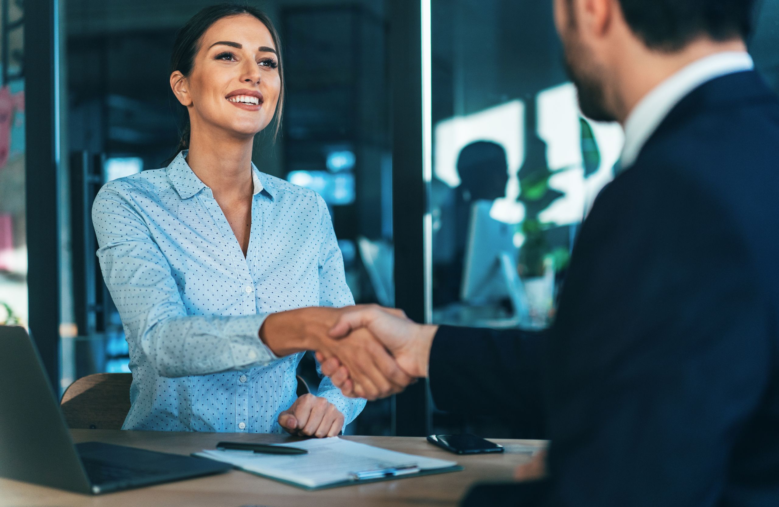 Woman smiling and shaking hands with a client across a desk